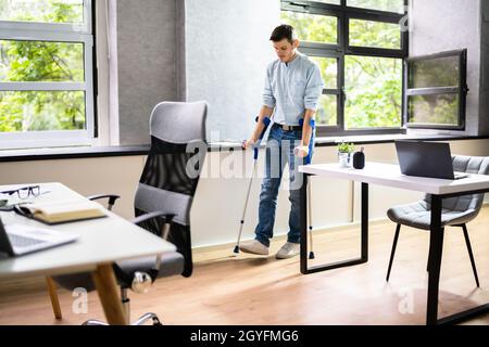 Arbeiter Mit Krücken Am Arbeitsplatz Oder Im Büro. Leistungen Für Die Rehabilitation Bei Handicap Stockfoto