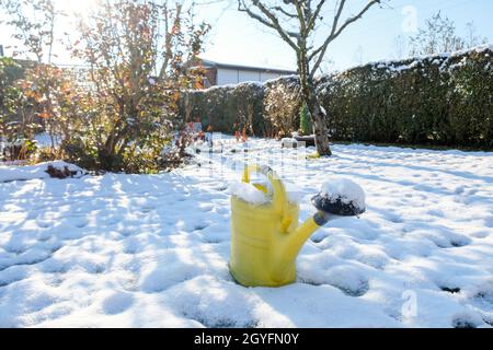 Im Winter steht im verschneiten Garten eine gelbe Gießkanne Stockfoto