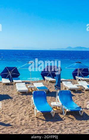 Entspannen Sie sich auf blauen Sonnenliegen im Urlaub auf Rhodos Griechenland mit dem wunderschönen klaren türkisfarbenen Wasser des Elli Strandes. Stockfoto