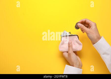 Frau, die Münzen in die Brieftasche auf gelbem Hintergrund legt Stockfoto