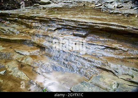 Das Wasser fließt sanft über einen steinigen Grund eines flachen Wasserbeckens, der kleine Wasserfälle bildet Stockfoto