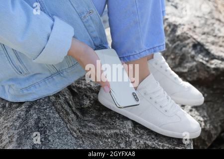 Frau, die im Freien beschädigtes Mobiltelefon aus Stein pflückt, Nahaufnahme Stockfoto