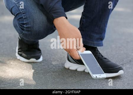 Mann pflückt beschädigtes Mobiltelefon aus der Nähe vom Straßenbelag im Freien Stockfoto