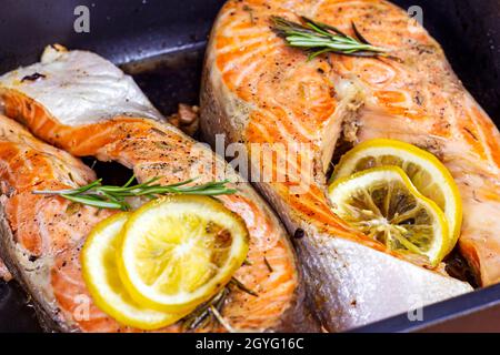 Frisch geröstete Fischsteaks aus rotem Lachs mit Kräutern, Gewürzen und Zitrone auf schwarzem Metallteller. Stockfoto