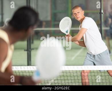 Fokussierter Padel-Spieler, der in engem Feld mit zwei Händen auf die Hinterhand trifft Stockfoto