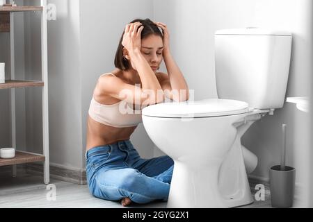 Junge Frau in der Nähe von Toilettenschüssel im Badezimmer. Anorexie-Konzept Stockfoto