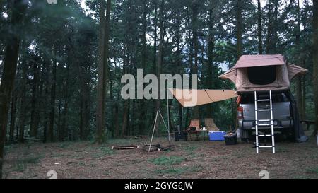 Pickup-Auto mit Zelt auf dem Dach und allein Mann Kochen im Wald. Abenteuer Reise Lifestyle Fernweh. Camping in der Wildnis Stockfoto