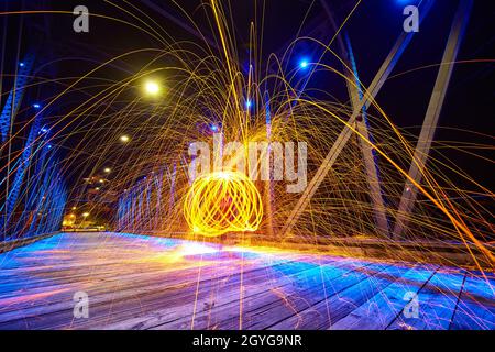 Gelbe Funken fliegen auf einer Brücke in der Nacht mit einer inneren Kugel aus mehreren Ringen aus gelbem Licht Stockfoto