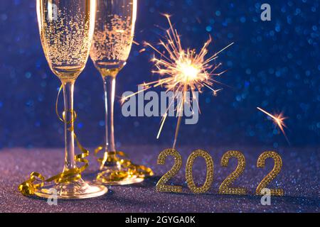 Frohes neues Jahr 2022.Weihnachten und Neujahr Urlaub Hintergrund mit zwei Tassen, ein Glas Champagner und Wunderkerzen auf blauem Hintergrund mit Bokeh Stockfoto