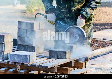 Ein Arbeiter mit einer Kreissäge schneidet in Nahaufnahme Pflasterplatten. Stockfoto
