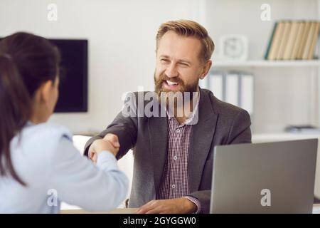 Glücklicher Mann, der bei einem Geschäftstreffen im Büro lächelt und einer Frau die Hände schüttelt Stockfoto