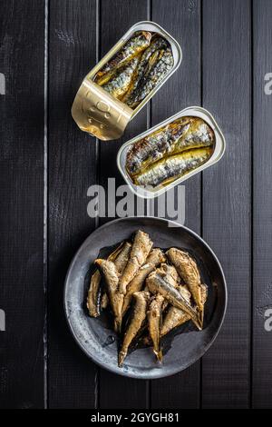 Sardinen und Sprotten aus der Dose. Seefisch in Zinndose auf schwarzem Tisch. Draufsicht. Stockfoto