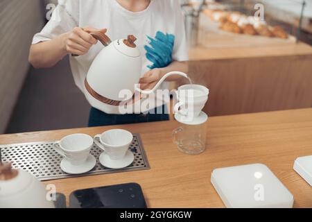 Weibliche Barista gießt gekochtes Wasser durch den Filter in den Glaskrug Stockfoto