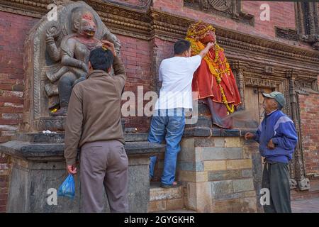 Vor dem alten königlichen Palast in Patan, Kathmandu Valley, Nepal, beten Männer an einer Statue von Kala Bhairav (l) und einer roten Figur von Hanuman an an Stockfoto