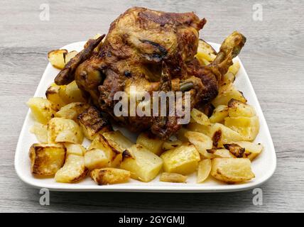 Ganz gebratenes Huhn mit Kartoffeln in einer weißen Schale auf einem Holztisch. Stockfoto