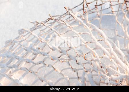 Abstraktes Winterfoto mit rostigen Käfig Rabitz bedeckt mit weißem Schnee an einem sonnigen Tag. Gebrochener Zaun in einem verlassenen russischen Dorf Stockfoto