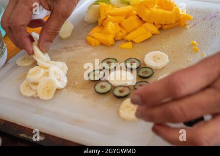 Hände legen Bananen- und Heidelbeerscheiben auf das Schneidebrett Stockfoto