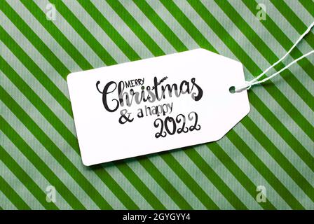 Label mit englischer Kalligraphie Frohe Weihnachten und Ein Happy 2022. Grünes Geschenkpapier Als Hintergrund Stockfoto