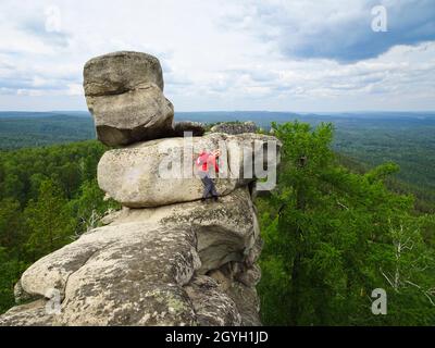 Eine junge Frau am Rande eines Abgrunds für ein schönes Foto. Gefahr von Touristenattraktionen. Mount Arakulskie Shikhany, Region Tscheljabinsk, Russland. Stockfoto