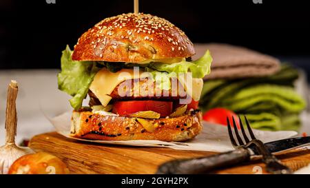 Appetitliche Hühnerburger mit Cheddar-Käse, frischem Salat und Gemüse auf einem Schneidebrett. Frische Salatblätter, Tomaten und Zwiebeln. Traditionelles A Stockfoto