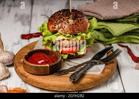 Hausgemachter appetitanreger Burger mit Fleischschnitzel, Käse, frischem Salat und Gemüse auf einem runden Schneidebrett. Salatblätter, Tomaten und Zwiebeln. Amerika Stockfoto