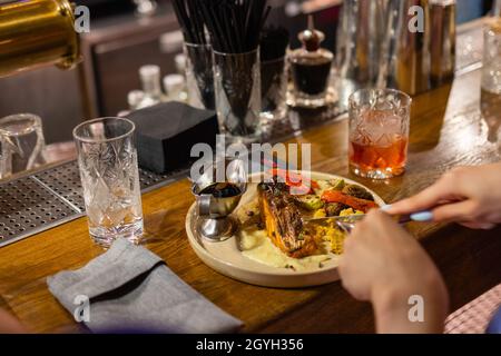 Junge Frau, die geröstetes Lachsfilet und Risotto mit Tintenfischen isst Stockfoto