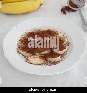 Kakaobeschichtete Bananenjause auf weißem Teller Stockfoto