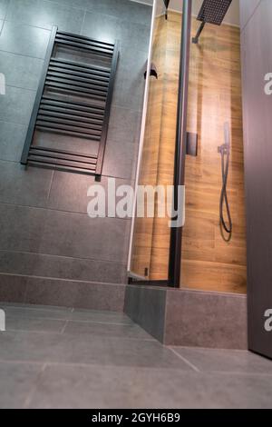 Blick auf die moderne gekachelte Dusche im Erdgeschoss mit großem rechteckigem Duschkopf und beheiztem Handtuchhalter an der Wand Stockfoto