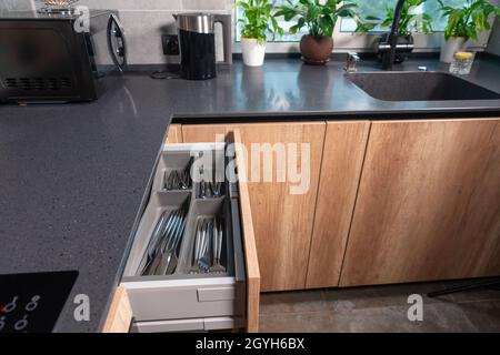 Offene Besteckschublade in einer modernen Einbauküche mit Holzschränken in einem Haus, in dem die ordentlich angeordneten Messer, Gabeln und Löffel in individuellen Komp Stockfoto