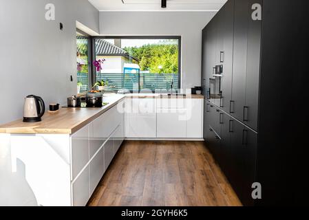 Eine moderne Küche mit weißen und schwarzen Fronten und einem großen Eckfenster, Vinylplatten auf dem Boden. Stockfoto