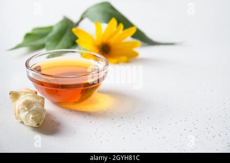 Jerusalemer Artischockensirup in Schale, Blumen und Wurzel auf weißem Hintergrund. Nahaufnahme. Speicherplatz kopieren. Stockfoto