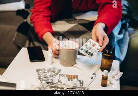 Beschnittenes Porträt eines kranken Jungen, der Pillen nahm. Verschiedene Pillen, Hustensirup, Nasenspray liegen auf dem Tisch. Medizinische Behandlung. Erkältung und Grippe, Allergie Stockfoto