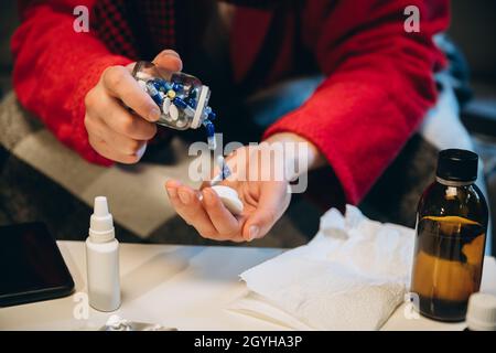 Beschnittenes Porträt eines kranken Jungen, der Pillen nahm. Verschiedene Pillen, Hustensirup, Nasenspray liegen auf dem Tisch. Medizinische Behandlung. Erkältung und Grippe, Allergie Stockfoto