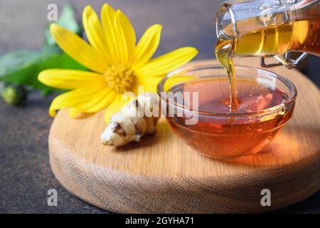 Gießen Jerusalem Artischockensirup in Schüssel, Blumen und Wurzel auf weißem Hintergrund. Nahaufnahme. Stockfoto