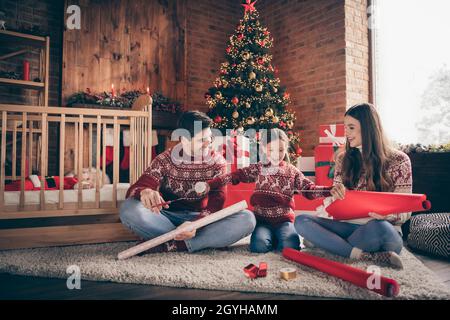 Foto von handlichen Menschen Familie sitzen Boden Vorbereitung Verpackung Geschenke tragen Pullover in dekorierten Weihnachten zu Hause drinnen Stockfoto