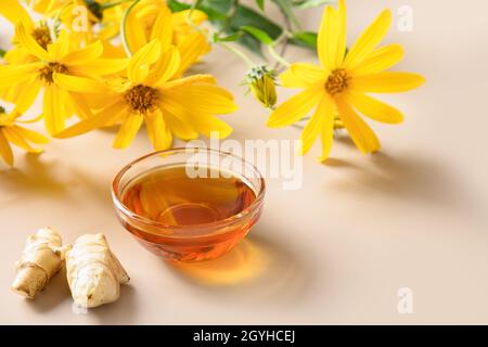 Jerusalemer Artischockensirup in Schale, Blumen und Wurzel auf beigem Hintergrund. Nahaufnahme. Speicherplatz kopieren. Stockfoto