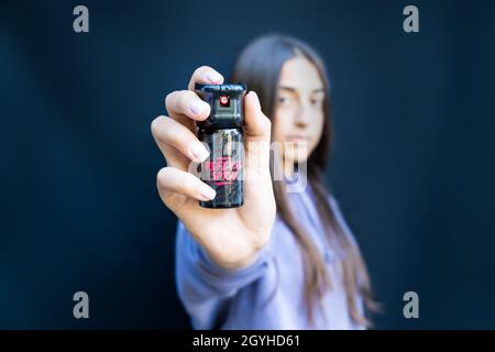 Selbstverteidigung von jungen Teenager-Mädchen mit Pfefferspray. Isoliert auf dunklem Hintergrund. Stockfoto