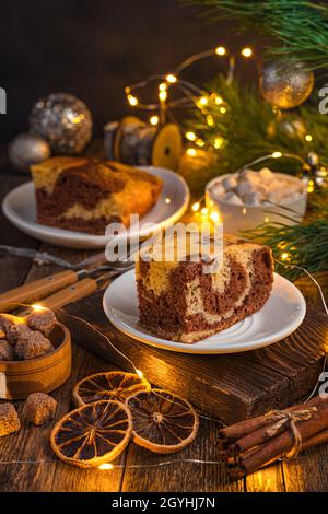 Ein Stück Kuchen auf festlichem Hintergrund im Licht einer Girlande. Das Konzept von Weihnachten, Neujahr. Seitenansicht, vertikal. Stockfoto