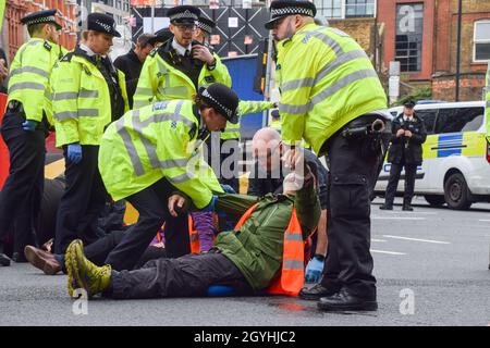 London, Großbritannien. Okt. 2021. Die Polizei entfernt und verhaftet britische Demonstranten, die sich am Kreisverkehr in der Old Street an die Straße geklebt haben. Beleidigung Großbritanniens die Demonstranten fordern, dass die Regierung bis 2025 alle sozialen Wohnungsbauten isoliert und die Verantwortung dafür übernimmt, dass alle Häuser im Vereinigten Königreich bis 2030 energieeffizienter sind, als Teil der umfassenderen Ziele für den Klimawandel und die Dekarbonisierung. Kredit: Vuk Valcic/Alamy Live Nachrichten Stockfoto