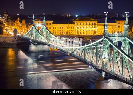 Freiheitsbrücke gegen das Corvinus-Universitätsgebäude in Budapest bei Nacht Stockfoto