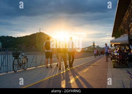 Menschen mit Hintergrundbeleuchtung, die bei Sonnenuntergang entlang der Uferpromenade spazieren Stockfoto