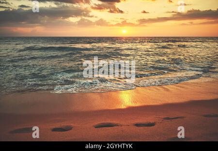 Szenischer Sonnenuntergang über dem Meer, Fußabdrücke auf dem Sand. Stockfoto