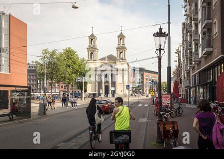 Radfahrer auf dem Radweg auf dem Waterlooplein mit der Moses- und Aaron-Kirche im Hintergrund in Amsterdam, Niederlande Stockfoto