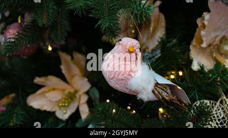 Festliche Weihnachtsbaumschmuck. Rosa Samtspielzeug Vogel und Hintergrund mit künstlichen Weihnachtssternen Blumen als Symbol für Weihnachten. Stockfoto