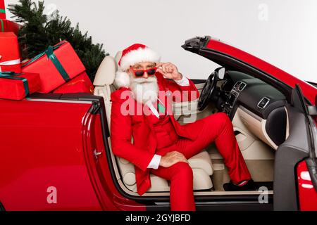 Foto von selbstbewussten stilvollen Look Großvater sitzen Automobil tragen Sonnenschutz Kostüm isoliert weiße Farbe Hintergrund Stockfoto