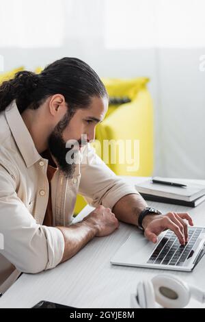 Serious hispanischen Mann mit Laptop in der Nähe verschwommene Notebooks auf dem Schreibtisch Stockfoto