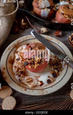 Frühstücksflocken im Herbst und Winter mit hausgemachtem, gebackenem Apfel, gefüllt mit Müsli und Joghurt. Serviert auf einem Teller auf einem Holztisch Stockfoto