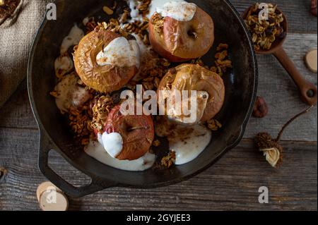 Hausgemachtes Frühstückszerealien mit frisch gebackenen Äpfeln und Müsli mit Zimt und Joghurt. Serviert auf rustikalem Holztisch. Stockfoto
