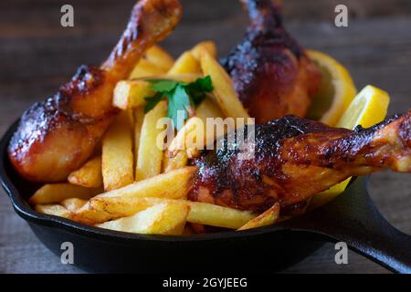 Marinierte Hähnchendrumsticks mit hausgemachten, frisch gebratenen pommes frites auf einem rustikalen Holztisch. Isolierte und Nahaufnahme Stockfoto