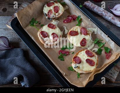 Im Ofen gebackene Sandwiches mit englischem Muffin und gekrönt mit irischem Cheddar-Käse und spanischer serrano-Salami. Stockfoto